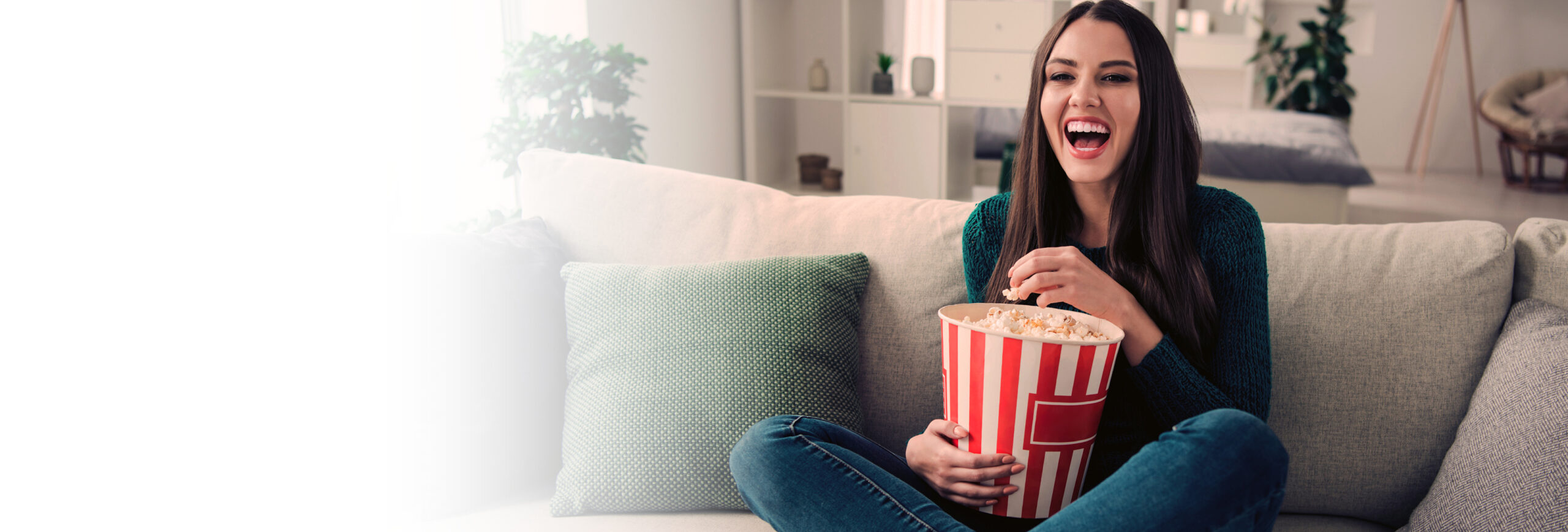 Girl sitting on couch eating popcorn and watching TV